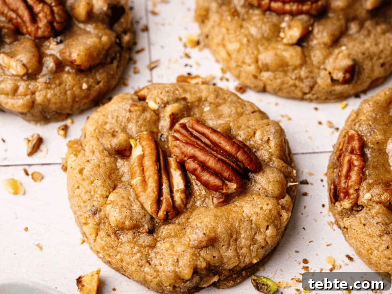 13 Christmas Cookies That Win Every Office Cookie Exchange 7 A hand holds a bitten Butter Pecan Cookie topped with a pecan and chopped nuts, with a blurred background.