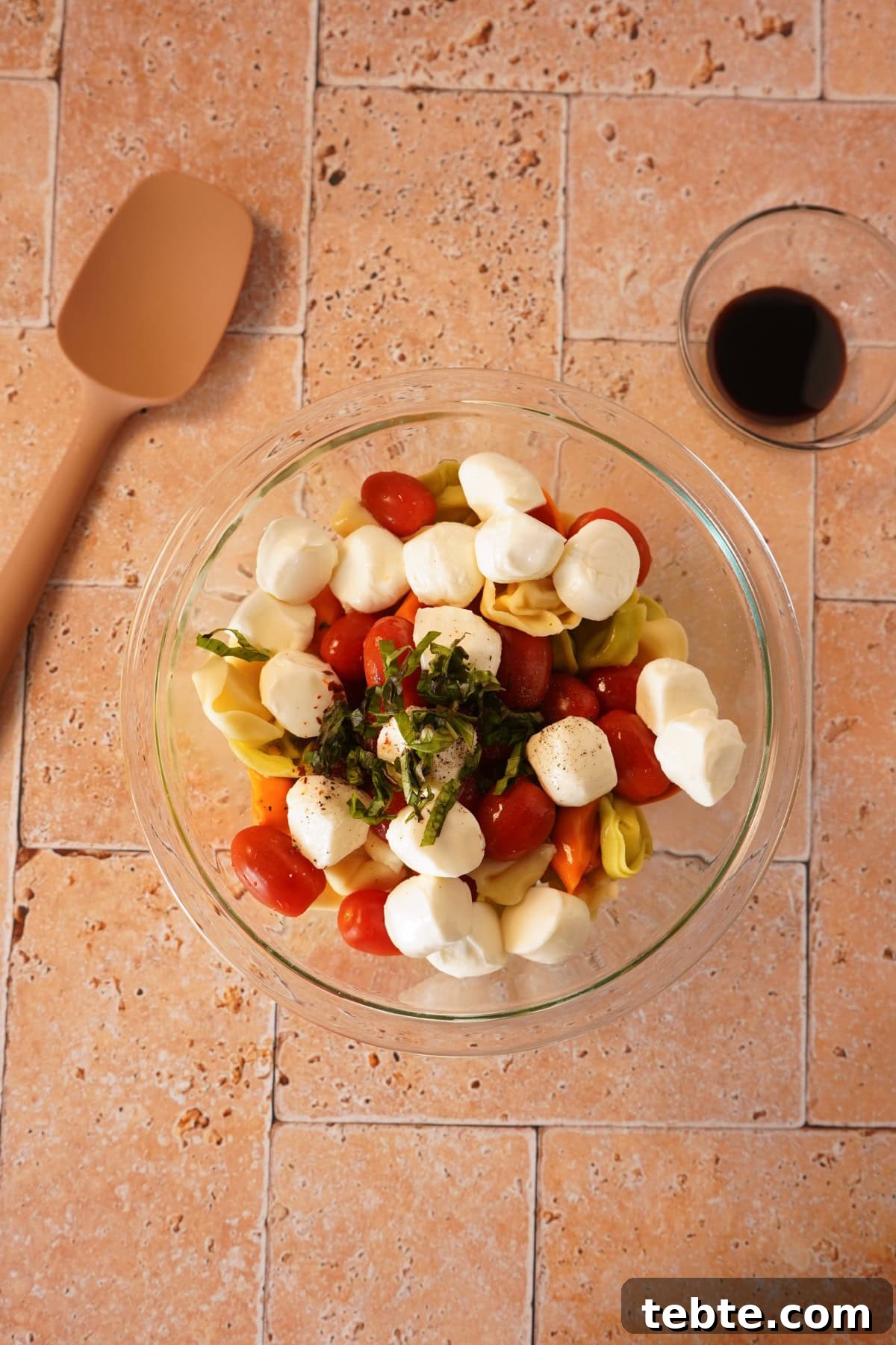 Caprese Tortellini Salad with Cherry Tomatoes & Basil 5 tortellini, tomatoes, mozzarella, and basil in glass bowl.