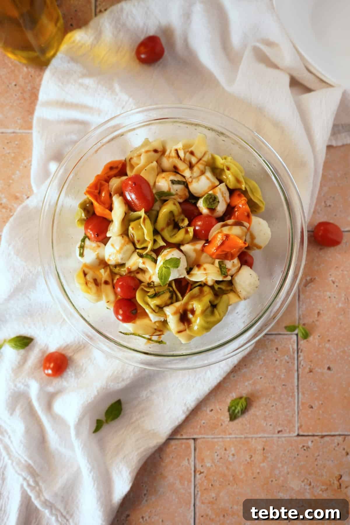 Caprese Tortellini Salad with Cherry Tomatoes & Basil 7 Tortellini pasta salad in bowl on white linen with balsamic glaze.