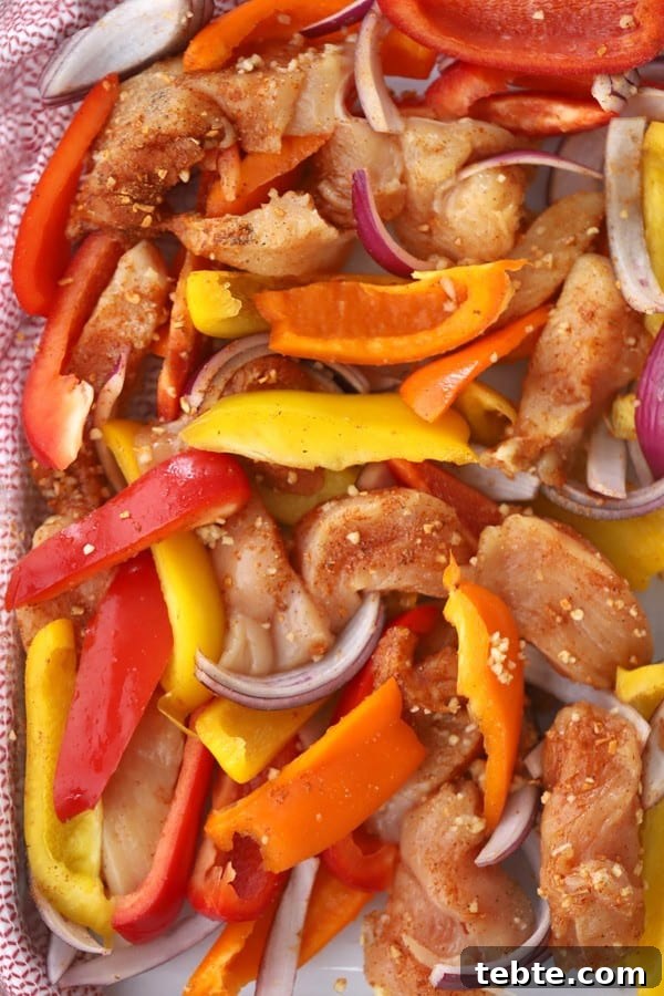 Sheet Pan Chicken Fajitas for Quick Weeknight Dinners 2 A sheet tray full of sliced chicken and peppers and onions for making baked chicken fajitas.
