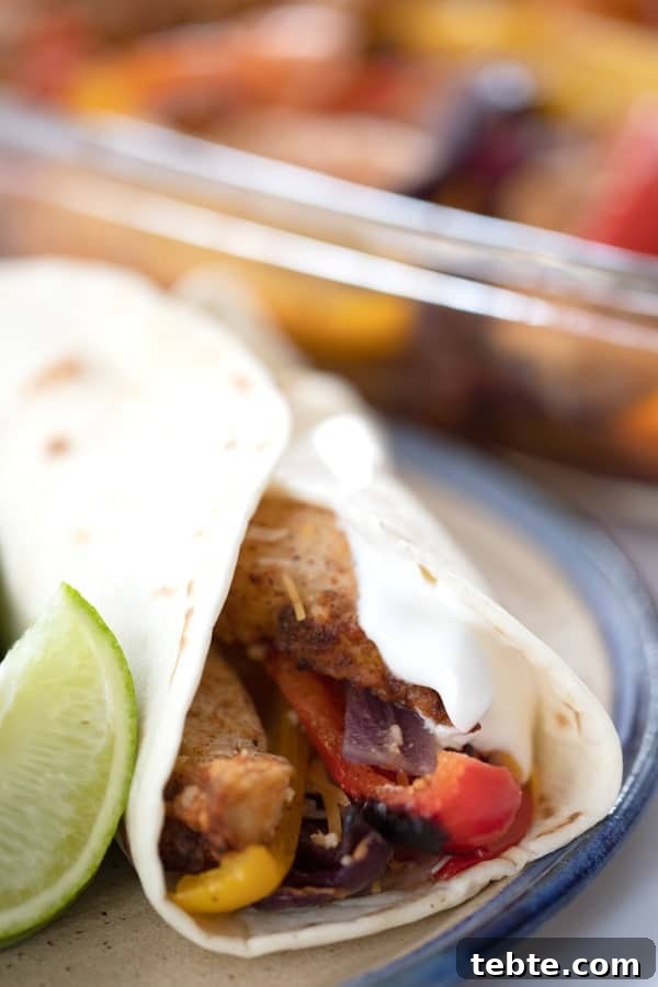 Sheet Pan Chicken Fajitas for Quick Weeknight Dinners 4 A tortilla full of oven baked chicken fajitas on a plate.