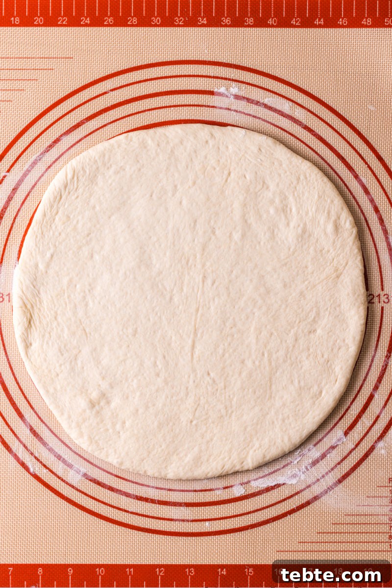 homemade pizza dough rolled out into a circle on a mat