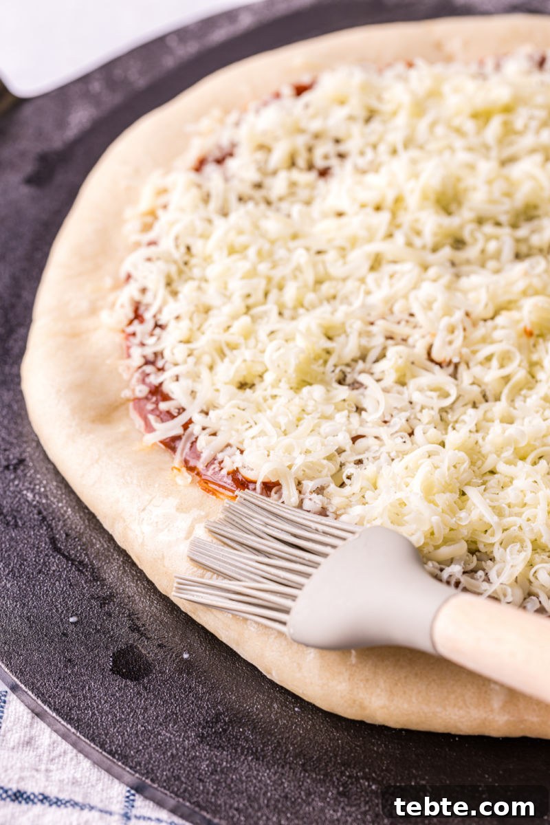 olive oil being brushed on the crust of an unbaked pizza