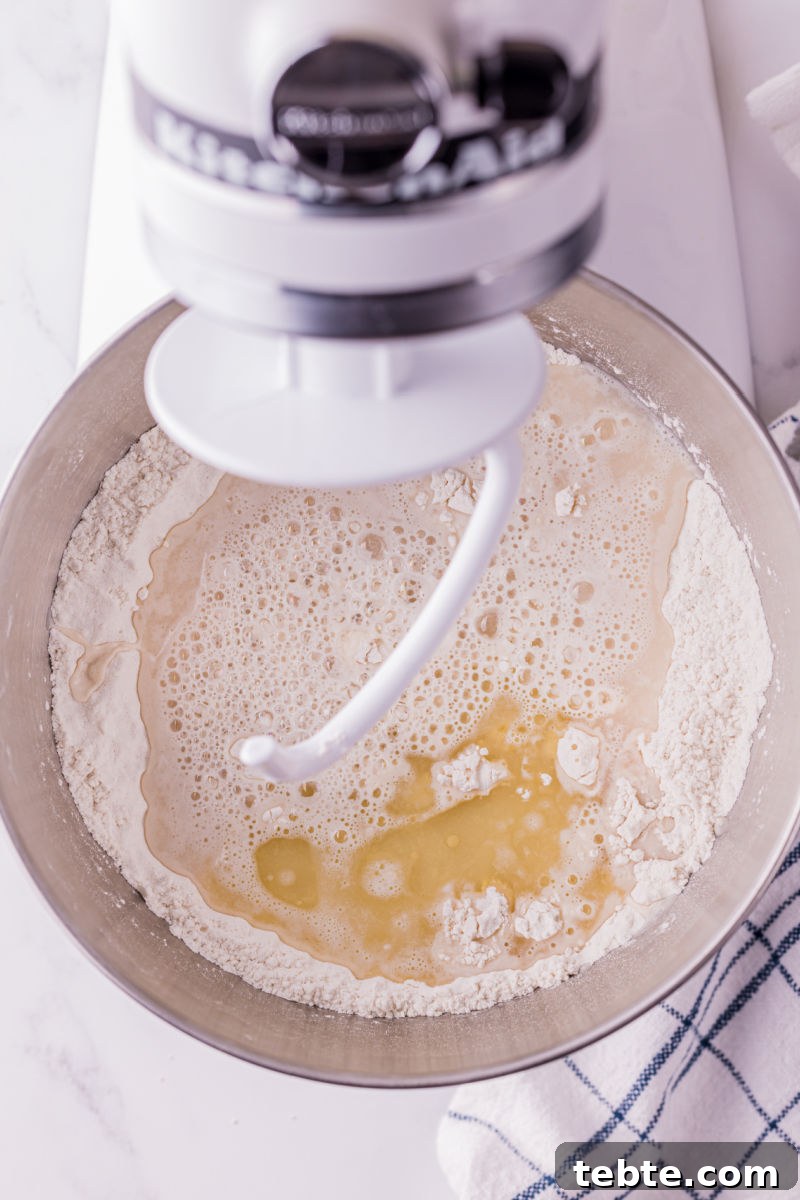 bloomed yeast mixture and olive oil poured into a stand mixer bowl with flour and salt