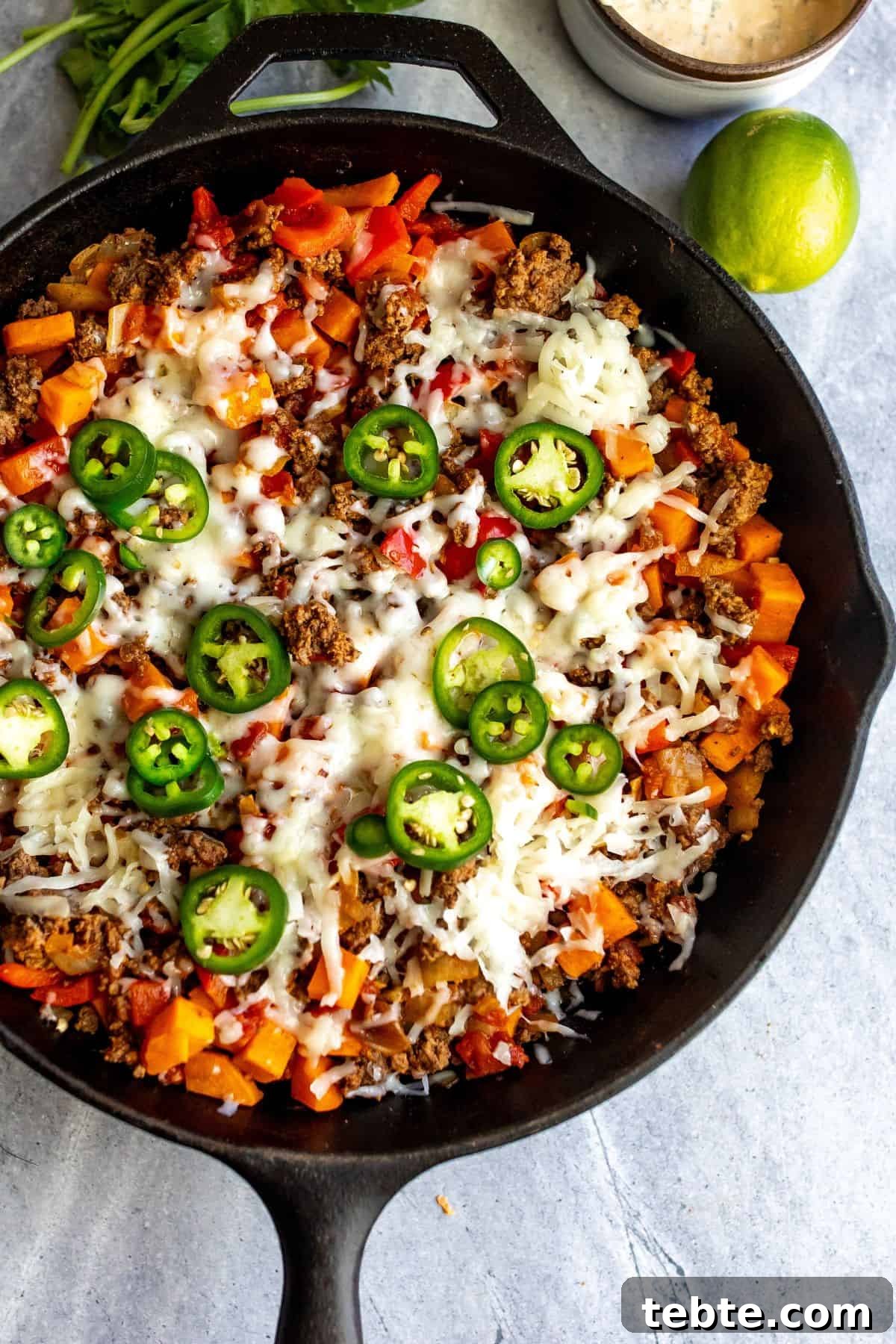 Cast iron skillet with beef and sweet potatoes and veggies. Melted cheese and avocado on top.