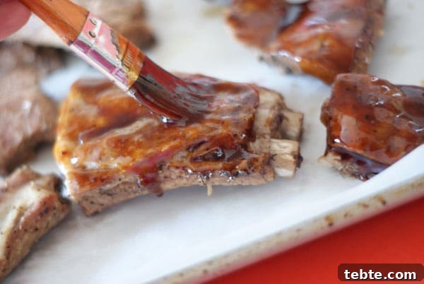 Orange Sticky Finger RIbs | Heather Likes Food brushing the sauce over the ribs on a baking sheet