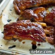 Sticky Orange-Glazed Pork Ribs — Tangy Asian-Style Recipe 3 sticky ribs on a baking sheet with sauce on them