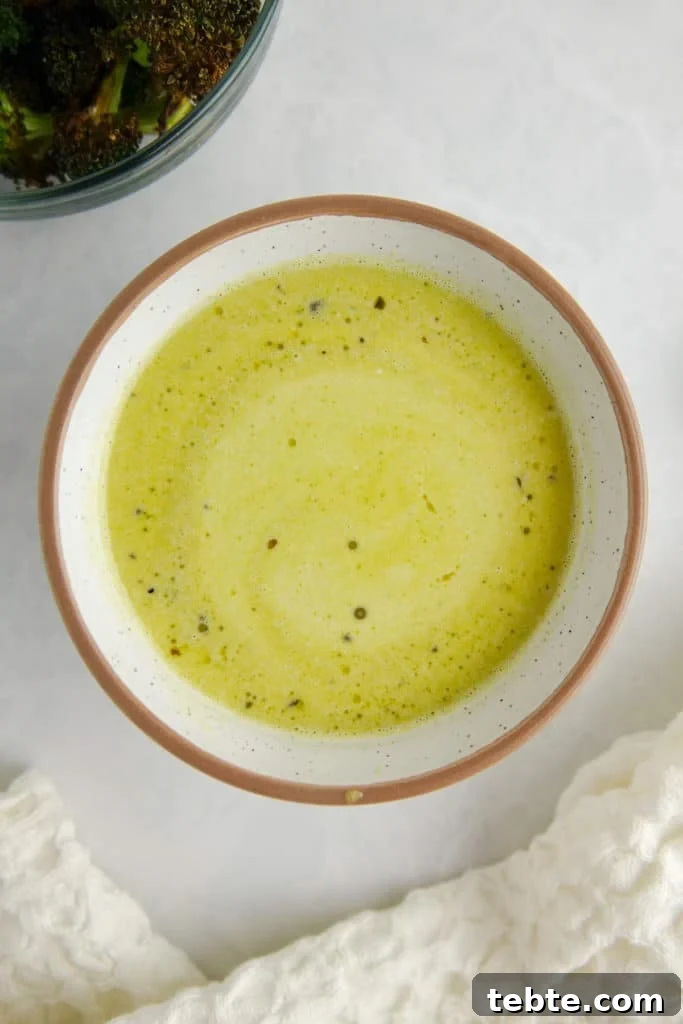 Creamy Pesto Vinaigrette Recipe for Salads, Pasta & Dips 2 Green salad dressing in a white ceramic bowl on a white marble counter, surrounded by a white kitchen towel and a bowl of broccoli