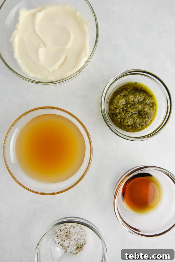 Creamy Pesto Vinaigrette Recipe for Salads, Pasta & Dips 3 Ingredients in glass bowls on a white marble counter, including mayonnaise, basil pesto, apple cider vinegar, maple syrup, and salt and pepper.