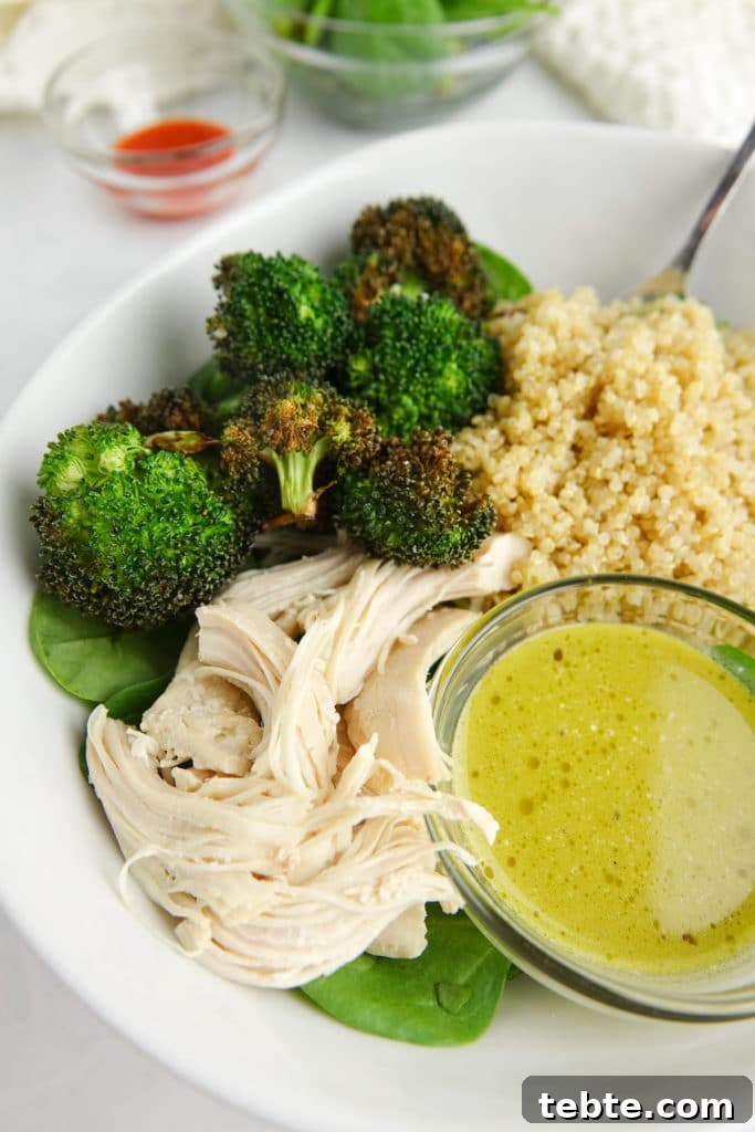 Creamy Pesto Vinaigrette Recipe for Salads, Pasta & Dips 4 Grain bowl in a white bowl, inculding quinoa, roasted broccoli, shredded chicken, spinach and green salad dressing.