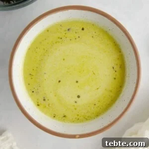 Creamy Pesto Vinaigrette Recipe for Salads, Pasta & Dips 5 Green salad dressing in a white ceramic bowl on a white marble counter, surrounded by a white kitchen towel and a bowl of broccoli