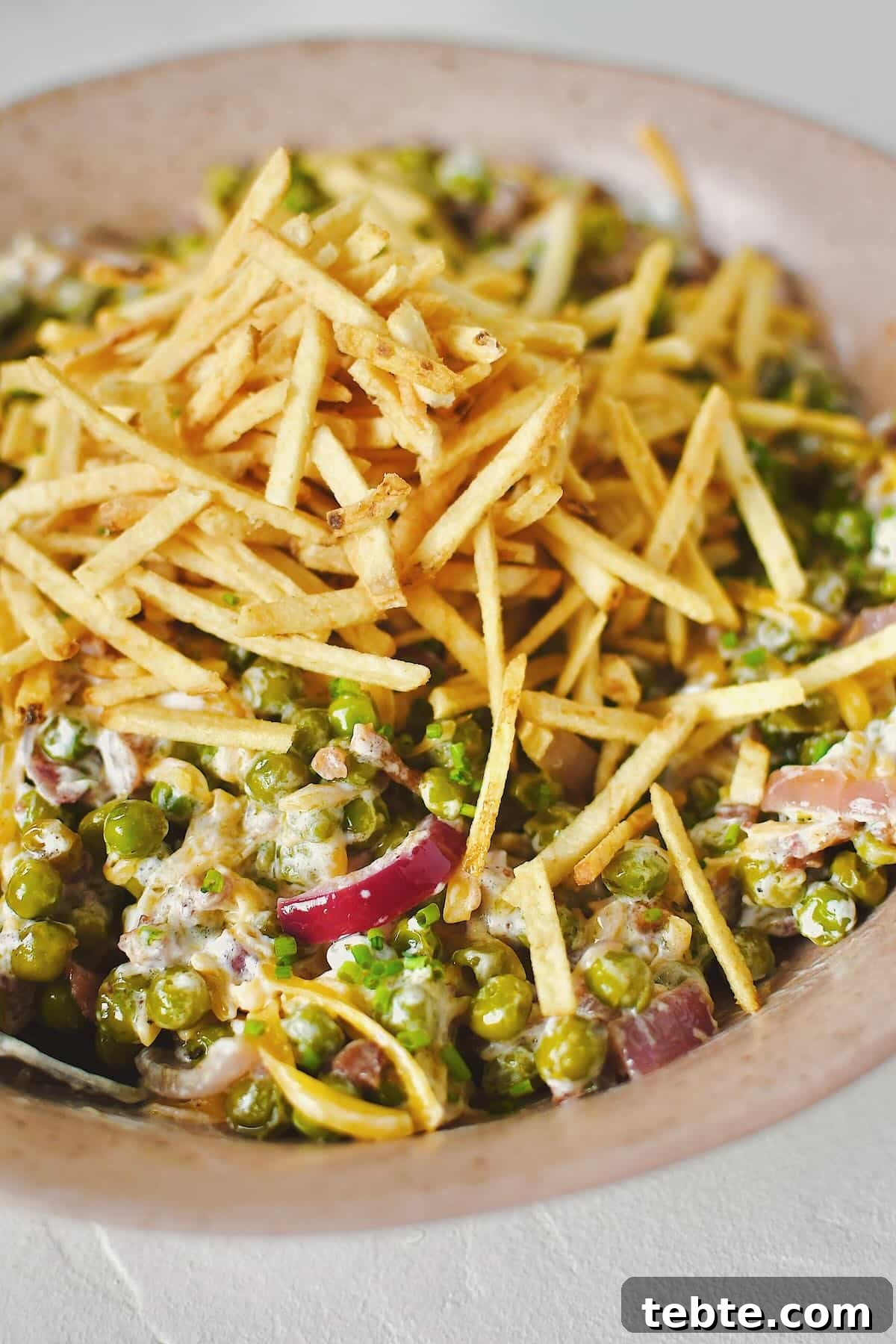 Creamy Pea Salad with Bacon and Red Onion 11 Bacon Pea Salad tossed together in a bowl and topped with shoestring potatoes.