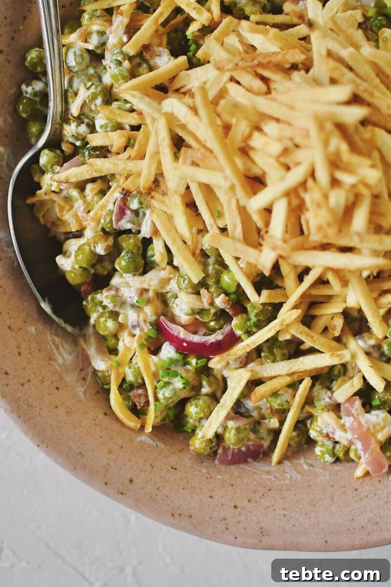Creamy Pea Salad with Bacon and Red Onion 8 Bacon Pea Salad tossed together in a bowl and topped with shoestring potatoes.