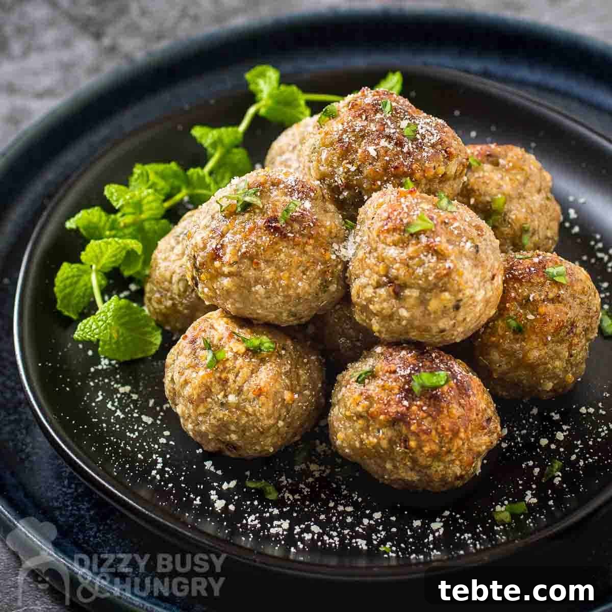 Crispy Air Fryer Turkey Meatballs with Garlic and Herbs 5 Side shot of multiple meatballs stacked on a black plate garnished with herbs and parmesan cheese.