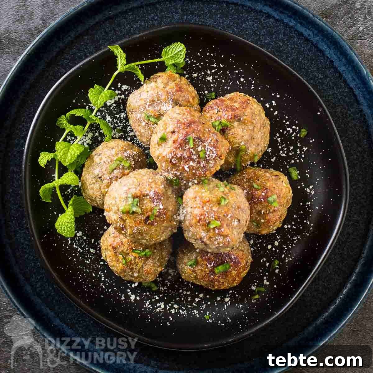 Crispy Air Fryer Turkey Meatballs with Garlic and Herbs 6 Overhead shot of multiple meatballs stacked on a black plate garnished with herbs and parmesan cheese.