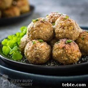 Crispy Air Fryer Turkey Meatballs with Garlic and Herbs 7 Side shot of multiple meatballs stacked on a black plate garnished with herbs and parmesan cheese with more meatballs in the background.