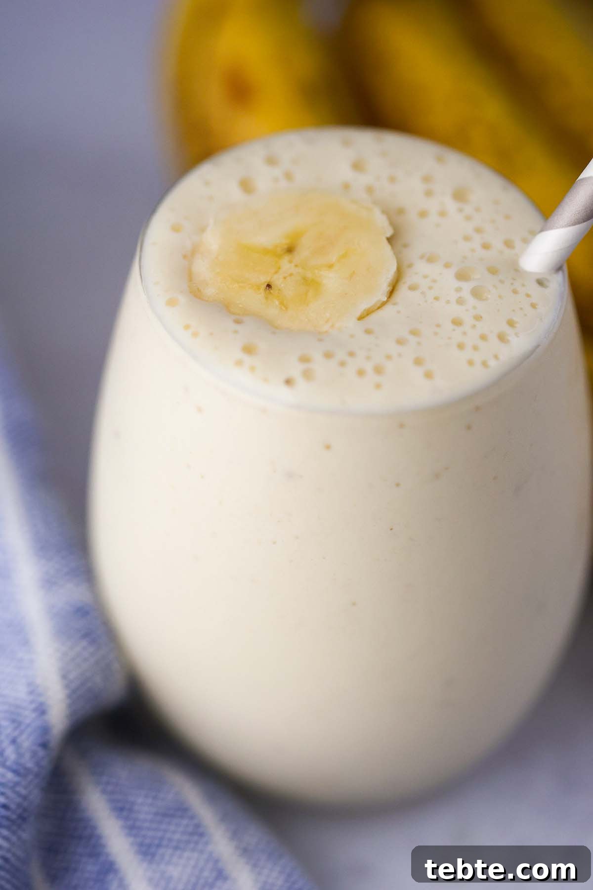 Creamy Banana Milkshake Recipe for Thick, Frosty Results 2 banana milkshake in a glass with a slice of banana on top and a straw.