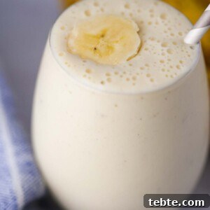 Creamy Banana Milkshake Recipe for Thick, Frosty Results 6 banana milkshake in a glass with a slice of banana on top and a straw.