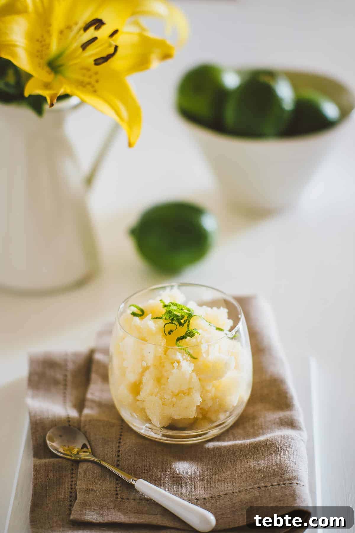 Refreshing Pineapple Granita Recipe: Tangy Frozen Dessert Guide 3 a glass filled with homemade pineapple granita on a cloth surrounded by limes and flowers