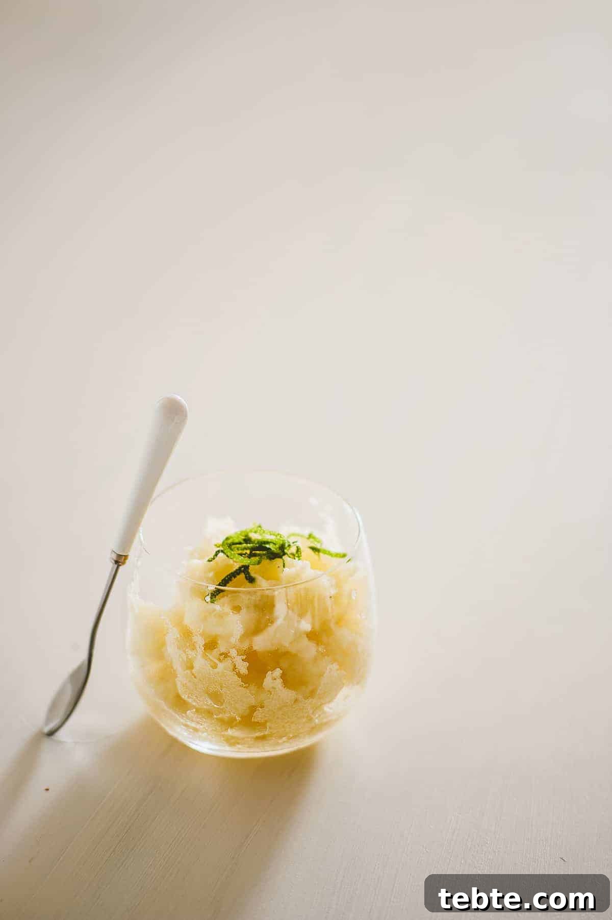 Refreshing Pineapple Granita Recipe: Tangy Frozen Dessert Guide 4 a glass on a white board filled with homemade pineapple granita with a spoon leaning against it