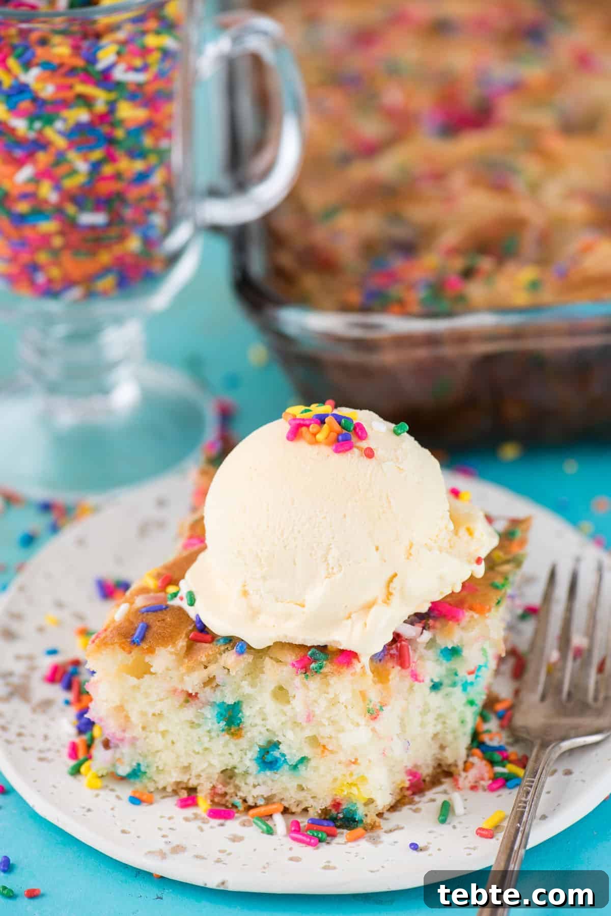 This funfetti earthquake cake is a white cake mix loaded with sprinkles and funfetti chocolate chips. Swirl in the cream cheese frosting layer and it bakes into the cake creating crevices and cracks on top of the cake. #earthquakecake #funfetticake #cake slice of funfetti earthquake cake with scoop of vanilla ice cream on white plate on blue background