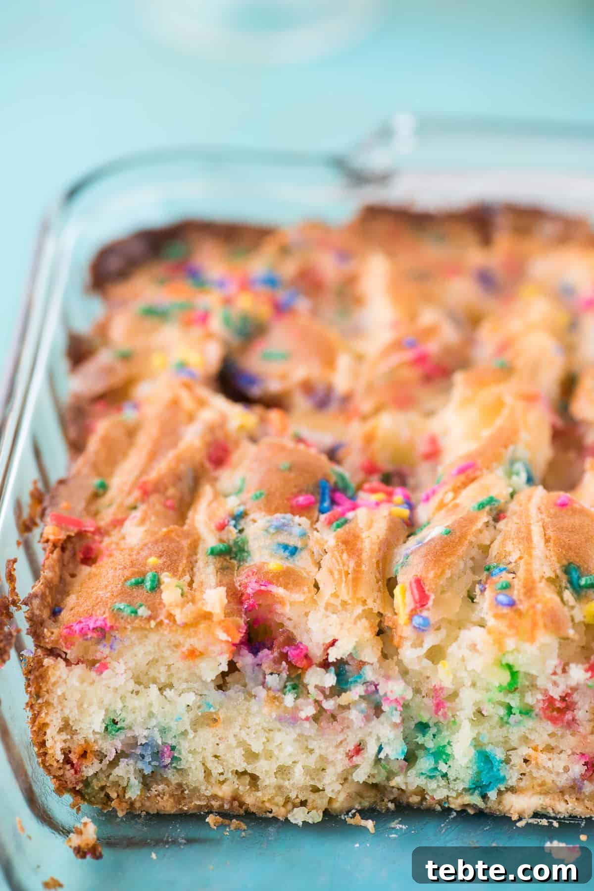 This funfetti earthquake cake is a white cake mix loaded with sprinkles and funfetti chocolate chips. Swirl in the cream cheese frosting layer and it bakes into the cake creating crevices and cracks on top of the cake. #earthquakecake #funfetticake #cake funfetti earthquake cake in glass 9x13 inch pan