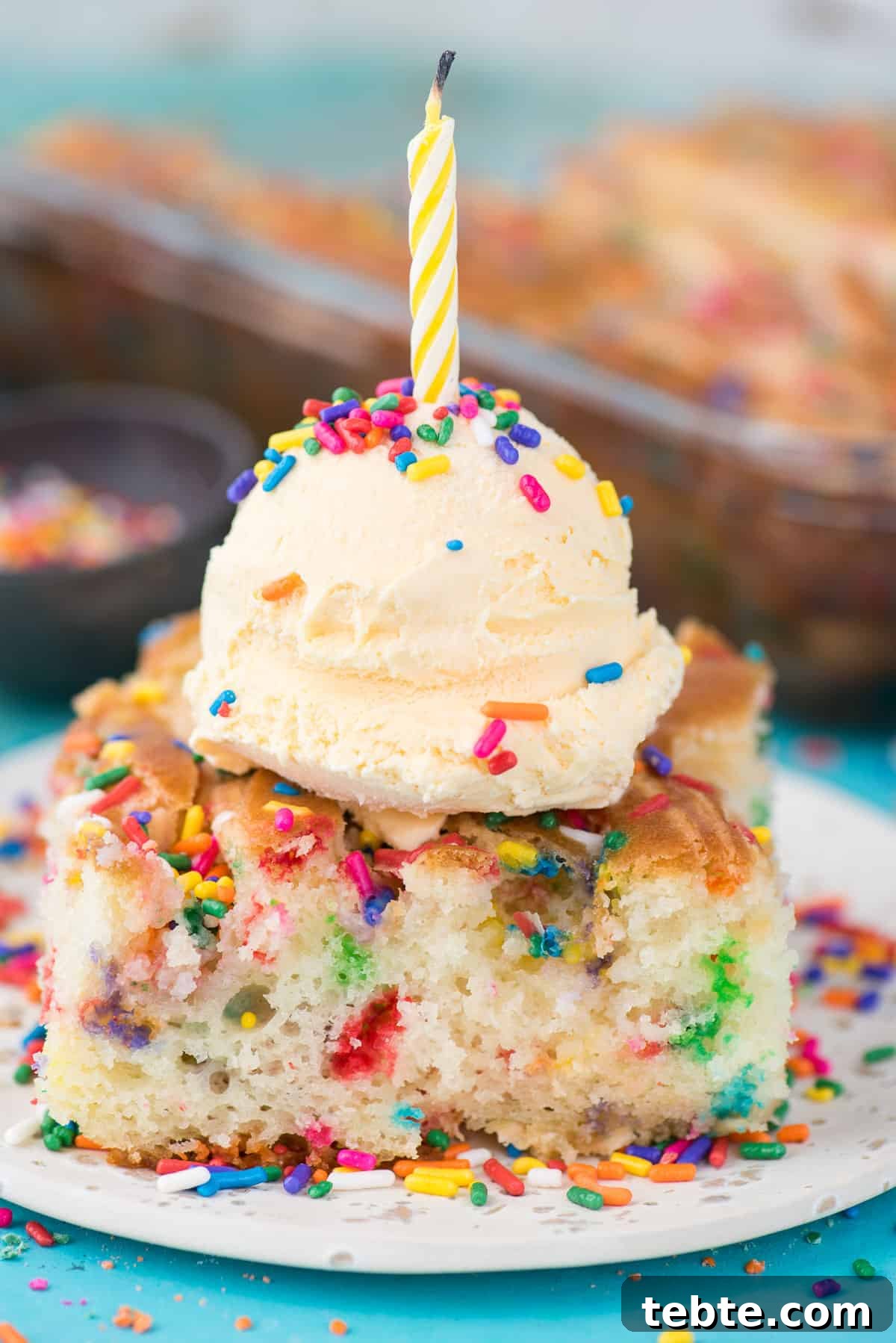 This funfetti earthquake cake is a white cake mix loaded with sprinkles and funfetti chocolate chips. Swirl in the cream cheese frosting layer and it bakes into the cake creating crevices and cracks on top of the cake. #earthquakecake #funfetticake #cake slice of funfetti earthquake cake with scoop of vanilla ice cream on white plate on blue background