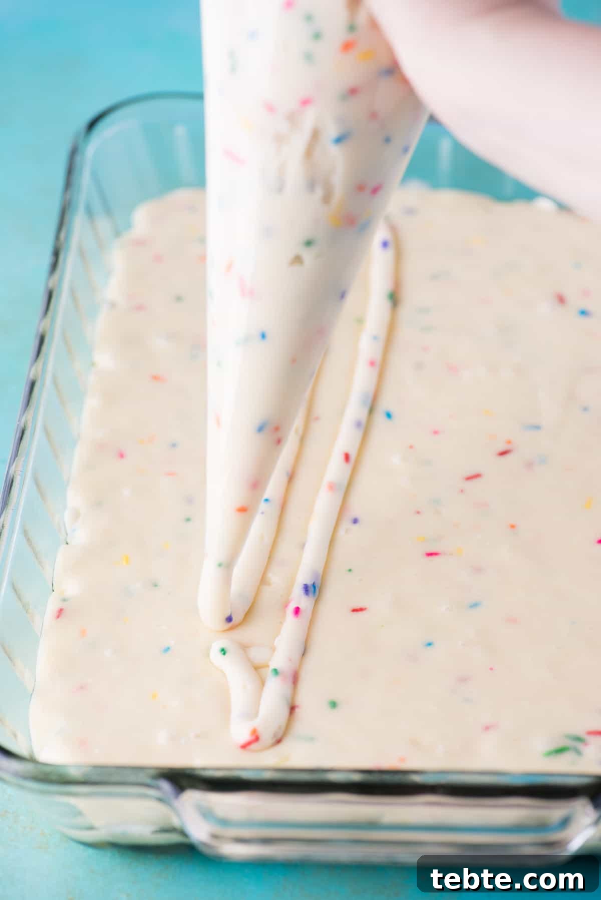 This funfetti earthquake cake is a white cake mix loaded with sprinkles and funfetti chocolate chips. Swirl in the cream cheese frosting layer and it bakes into the cake creating crevices and cracks on top of the cake. #earthquakecake #funfetticake #cake piping cream cheese filing on top of white cake mix in glass 9x13 inch pan