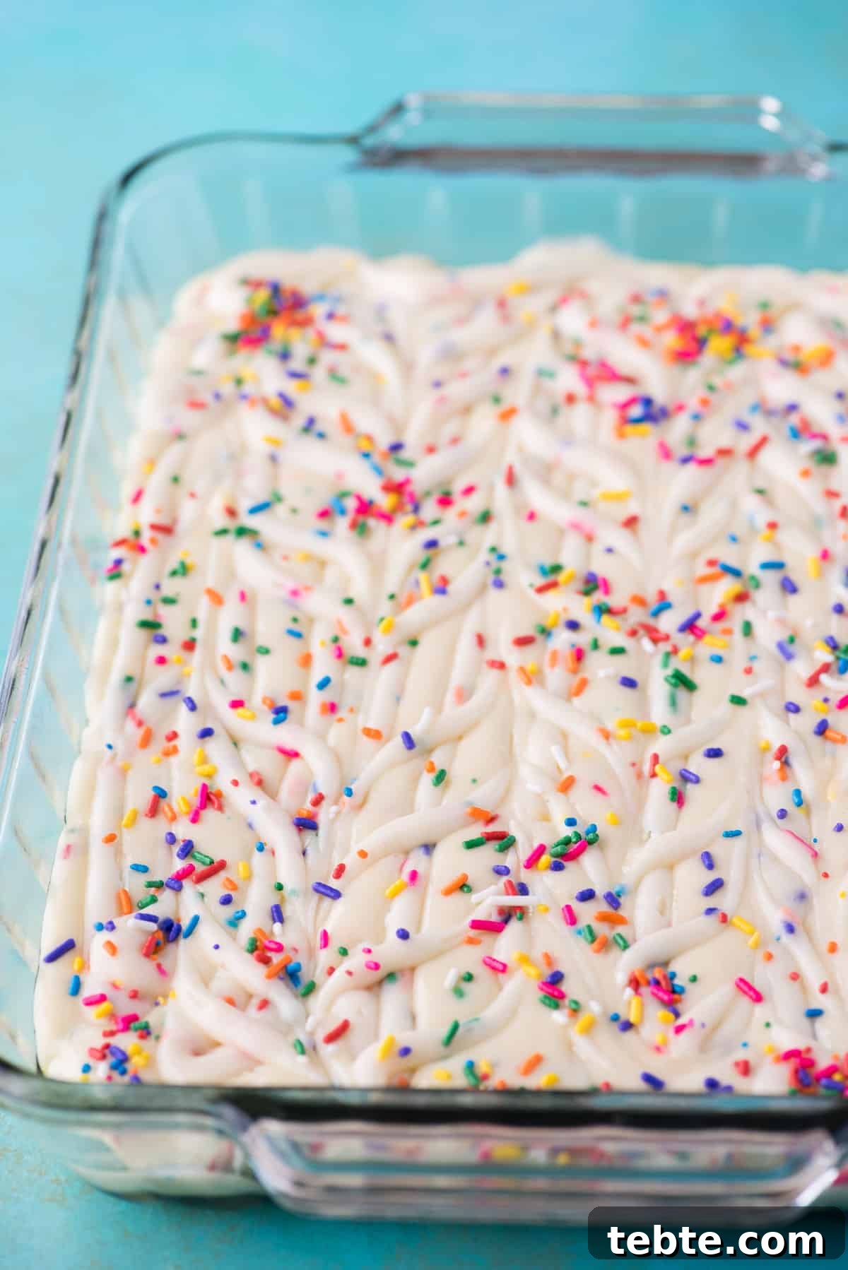 This funfetti earthquake cake is a white cake mix loaded with sprinkles and funfetti chocolate chips. Swirl in the cream cheese frosting layer and it bakes into the cake creating crevices and cracks on top of the cake. #earthquakecake #funfetticake #cake funfetti earthquake cake batter in glass 9x13 inch pan