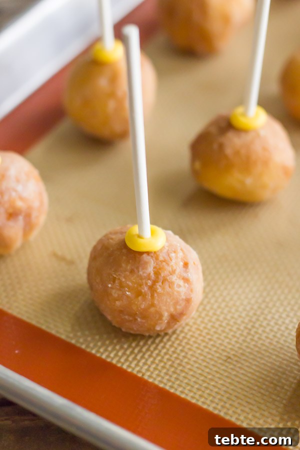 Donut holes with lollipop sticks pressed into them, on a Silpat lined baking sheet.