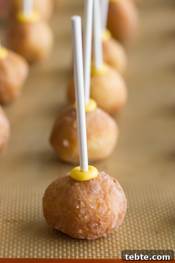 Donut holes with lollipop sticks pressed into them, on a Silpat lined baking sheet.