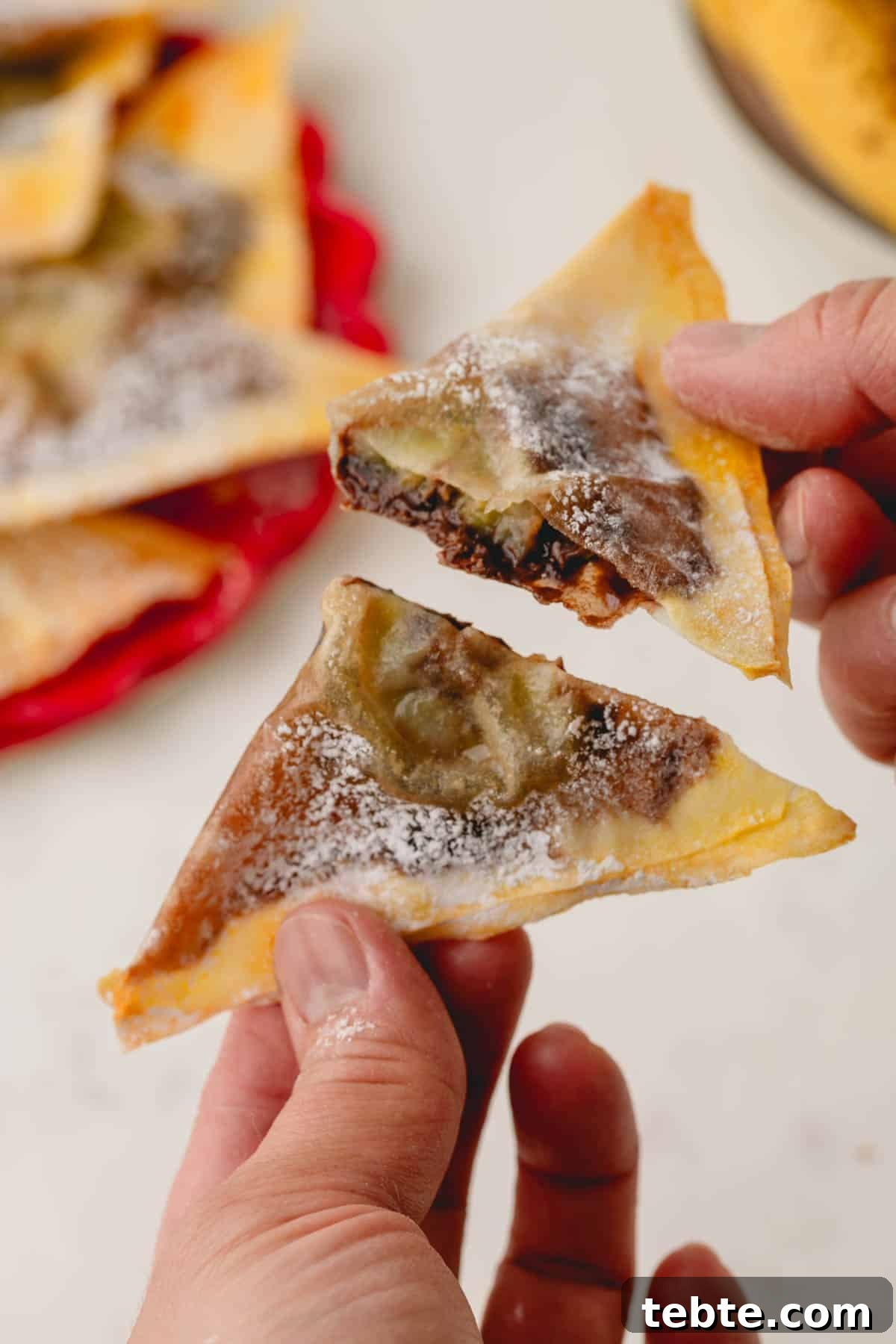 Crispy Banana and Nutella Wontons Recipe for Dessert Delight 3 Two hands, each holding a half of a banana Nutella wonton.