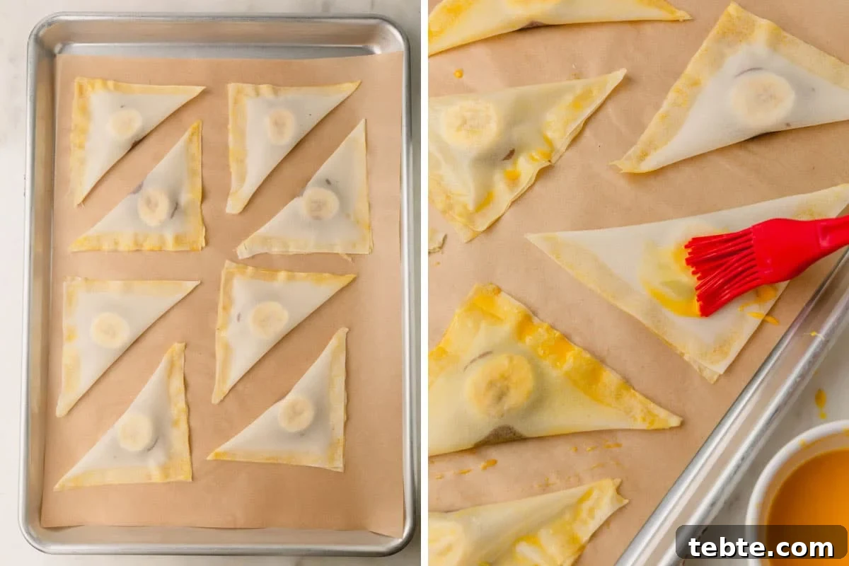 Crispy Banana and Nutella Wontons Recipe for Dessert Delight 6 Banana Nutella wontons on a parchment paper lined baking sheet being brushed with egg wash.
