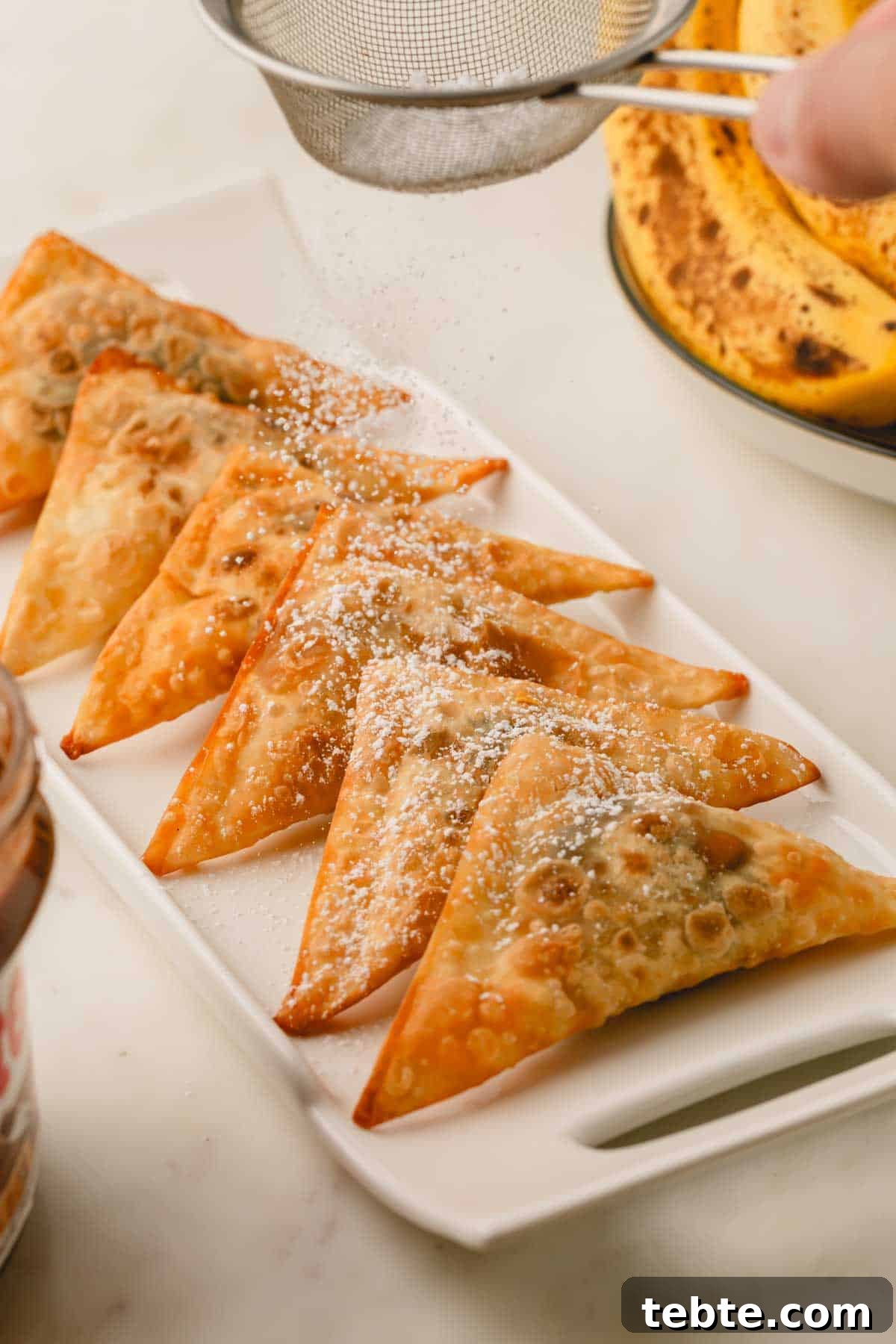 Crispy Banana and Nutella Wontons Recipe for Dessert Delight 9 A platter of banana and Nutella wontons topped with powdered sugar being dusted over the top.