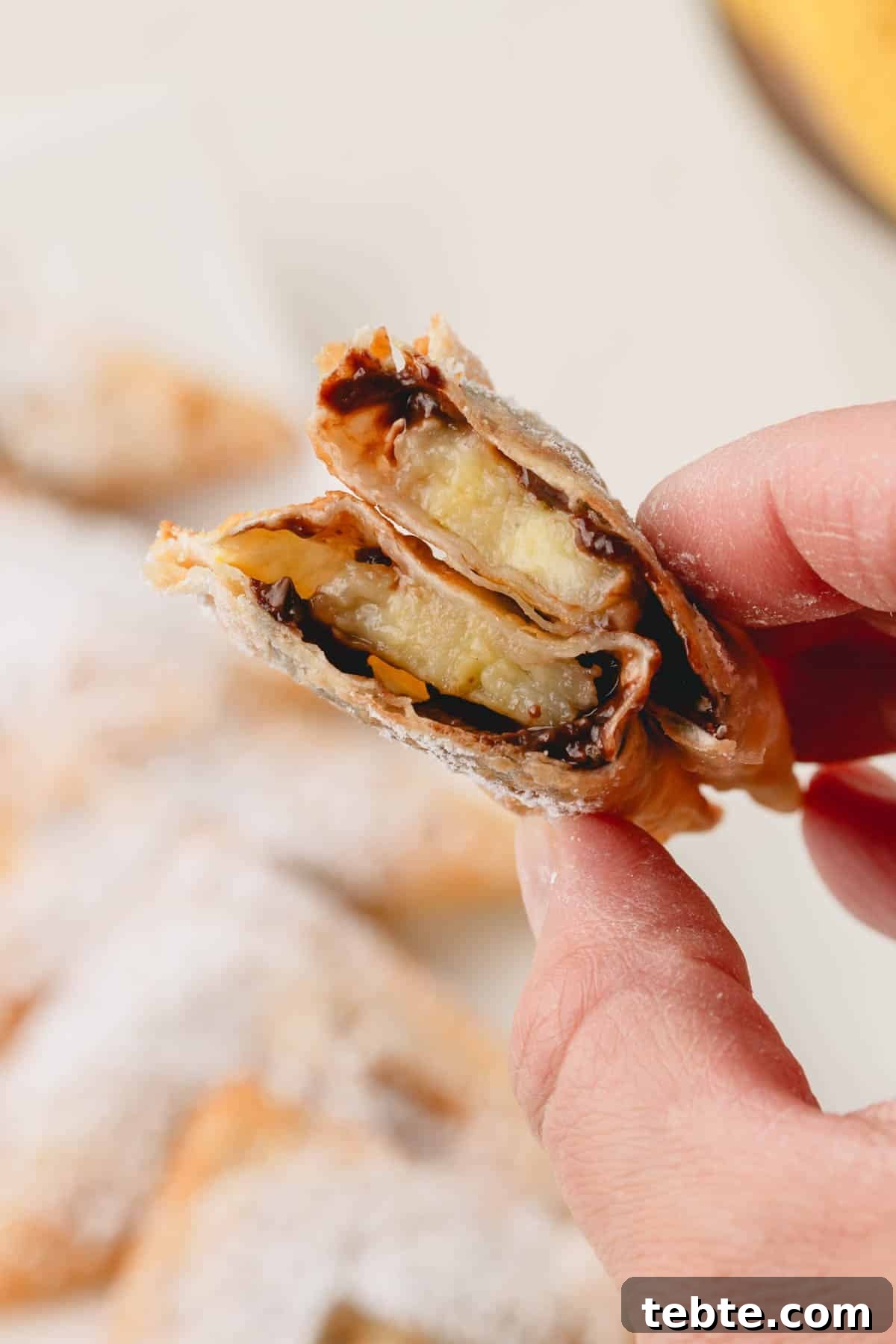 Crispy Banana and Nutella Wontons Recipe for Dessert Delight 10 A hand holding a banana Nutella wonton split in half.