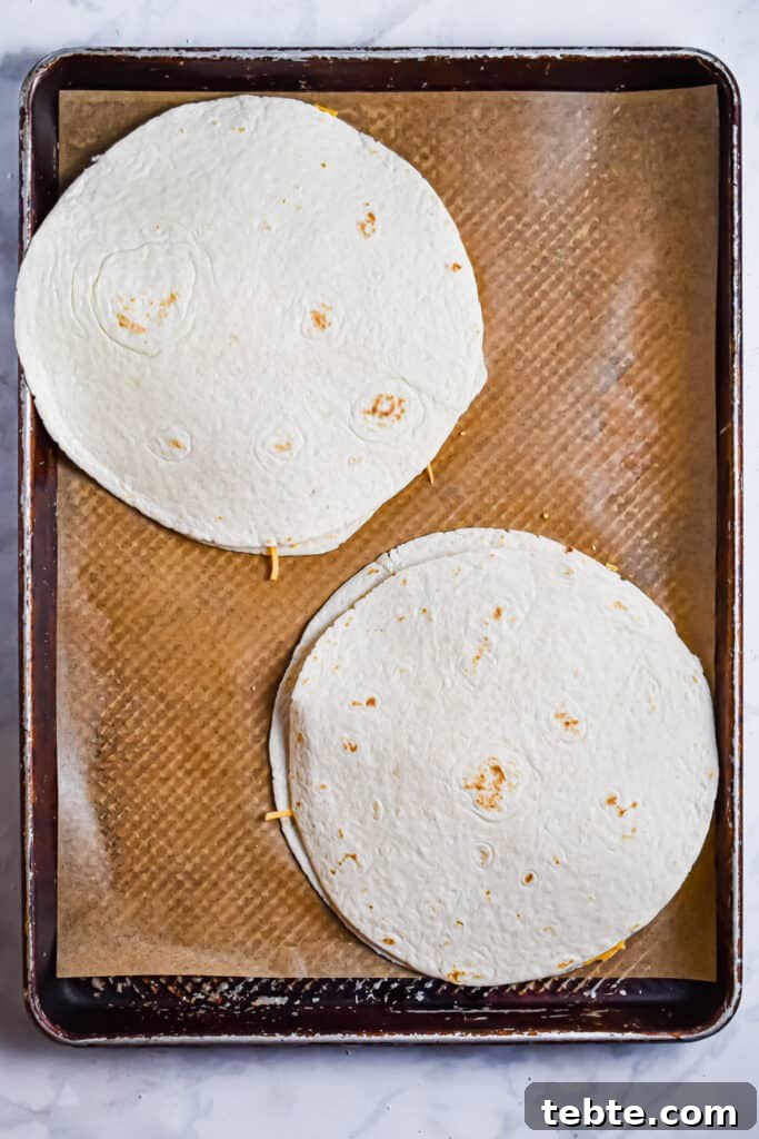The chicken and cheese is topped with another tortilla for the buffalo chicken sheet pan quesadillas