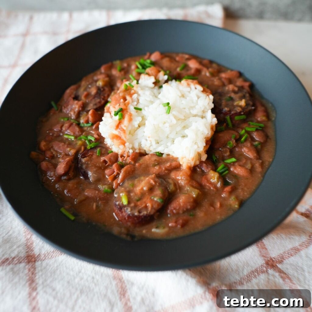 Authentic New Orleans Red Beans and Rice Recipe 2 Bowl of red beans and rice with sliced sausage, garnished with chopped chives and parsley on top of fluffy white rice.