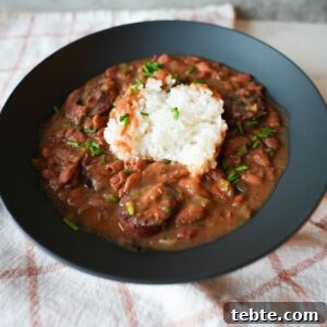 Authentic New Orleans Red Beans and Rice Recipe 7 Bowl of red beans and rice with sliced sausage, garnished with chopped chives and parsley on top of fluffy white rice.