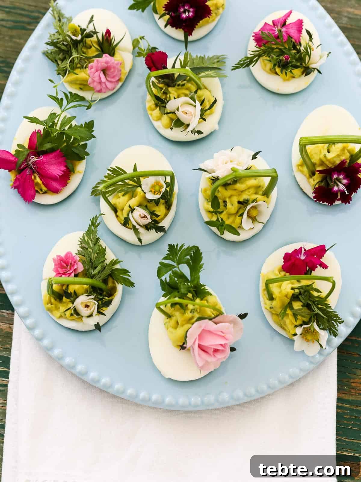 80+ Easter Dinner Menu Ideas for Every Guest and Occasion 4 Looking down into a pastel blue egg shaped plate loaded with deviled eggs for Easter decorated with edible flowers and herbs.