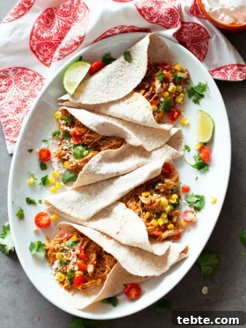4 tacos filled with shredded salsa chicken, lime and salsa on plate.