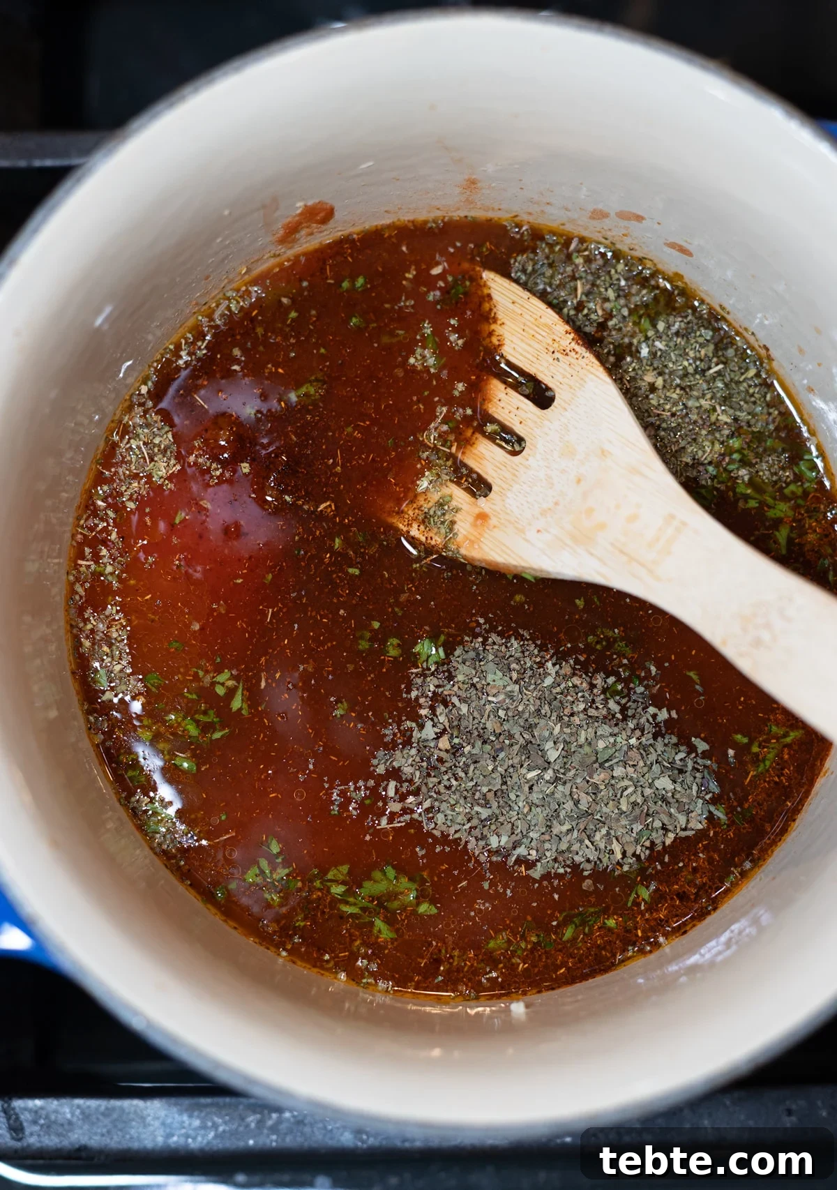 Homemade Red Enchilada Sauce Recipe for Authentic Flavor 6 Person adding herbs to a pan that has the tomato sauce and water.