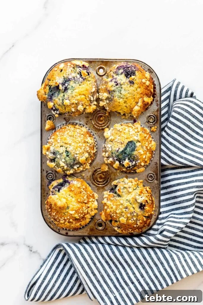 Why Are Blueberries Turning Green in Muffins? 4 A vintage muffin pan with freshly baked blueberry streusel muffins with a stripped blue and white kitchen linen