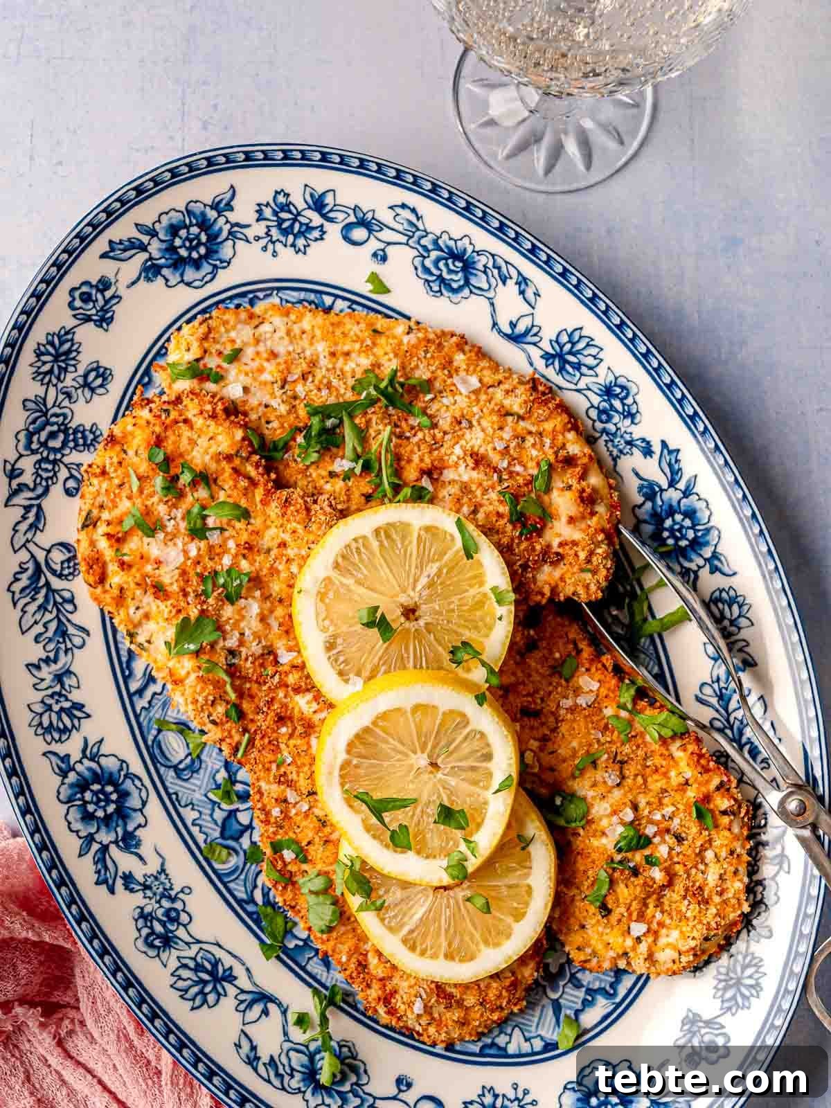 Golden, crispy air fryer parmesan-crusted chicken served on a decorative blue and white plate, garnished with lemon slices and fresh parsley.