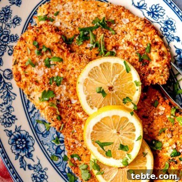 Parmesan-crusted chicken on a blue and white plate, garnished with lemon slices.