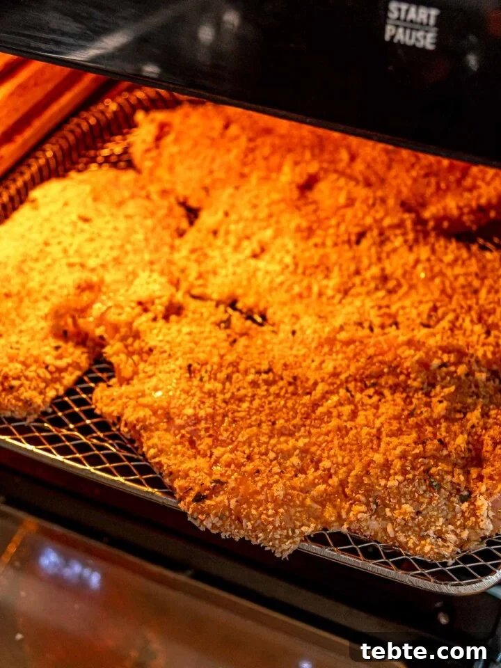 Breaded chicken breasts arranged in an air fryer, beginning to crisp up as they cook.