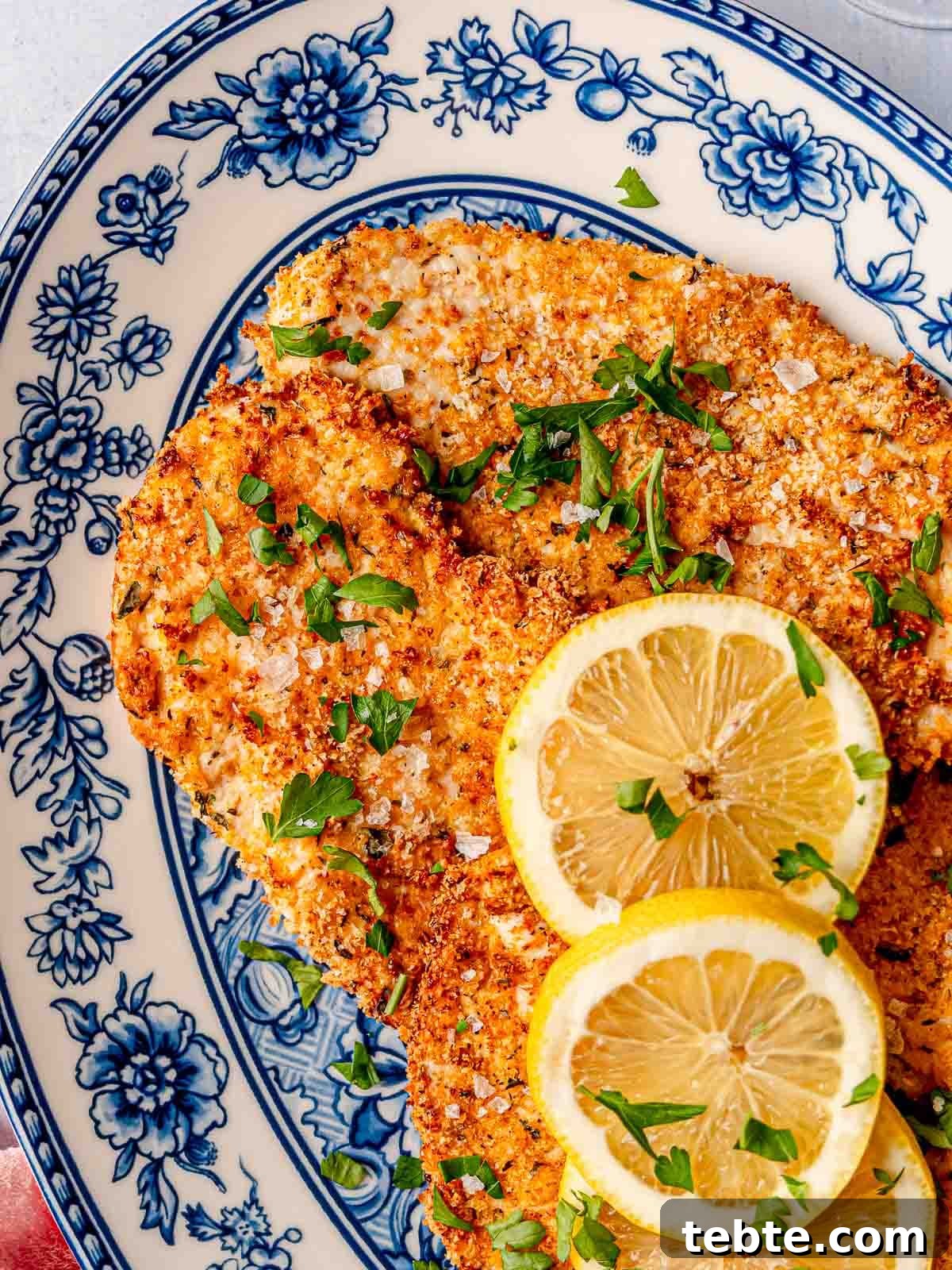 A close-up of crispy air fryer parmesan-crusted chicken, topped with lemon slices and fresh parsley, showing its crunchy texture