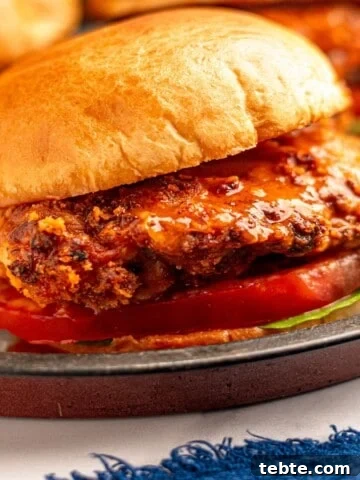 Close up view of a crispy buffalo chicken sandwich on a bun with lettuce and tomato.