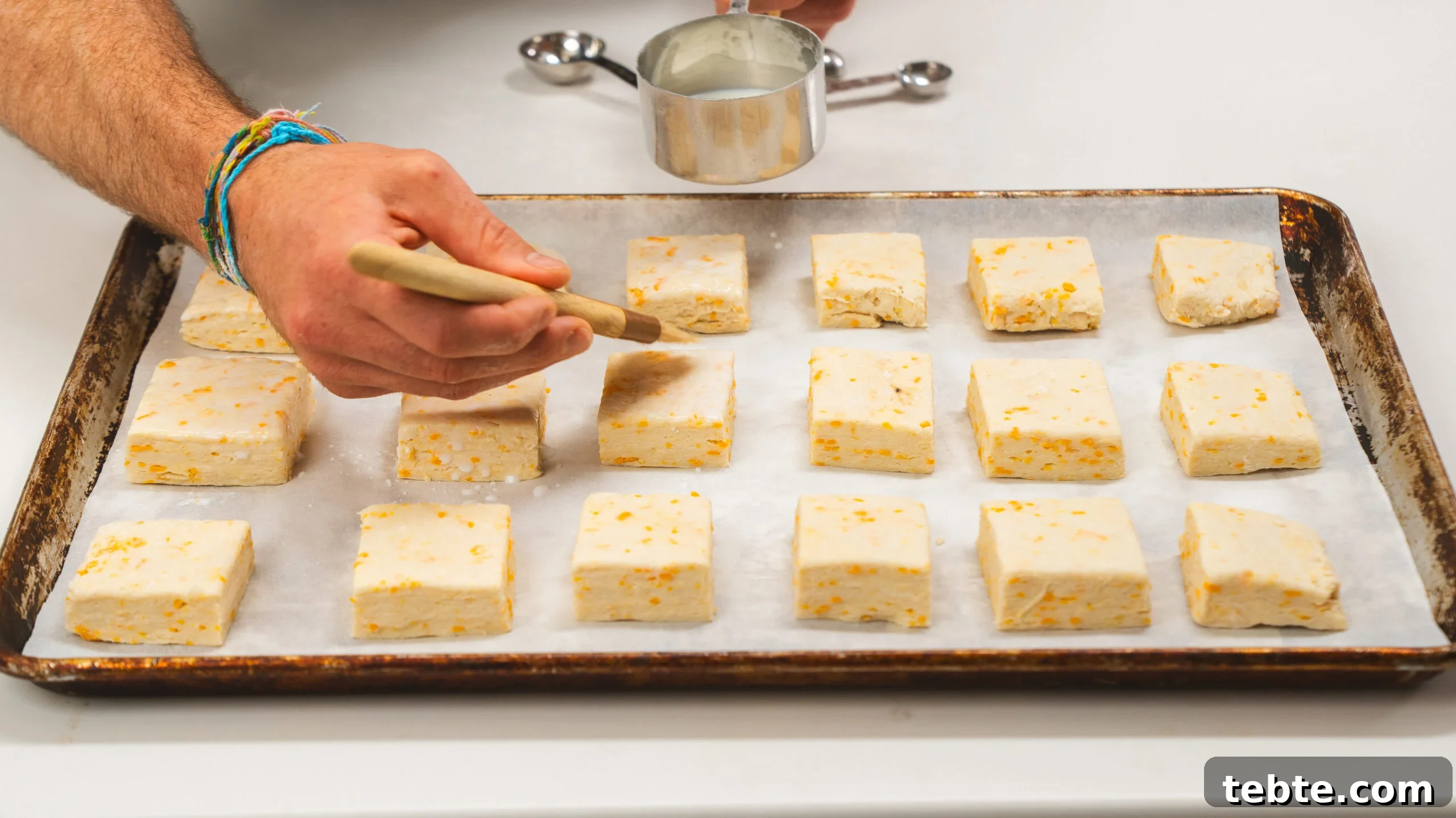Buttermilk biscuits on a parchment lined baking sheet being brushed with buttermilk.