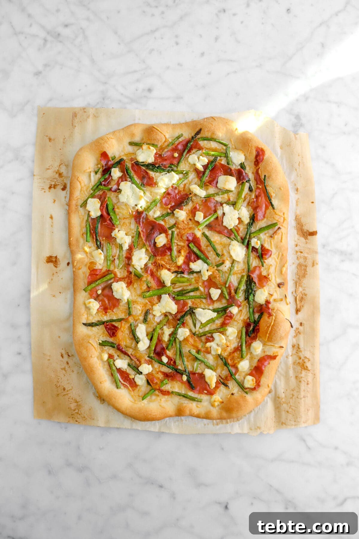 Asparagus, Caramelized Onion & Prosciutto Flatbread with Goat Cheese 18 baked asparagus and prosciutto flatbread on marble surface.