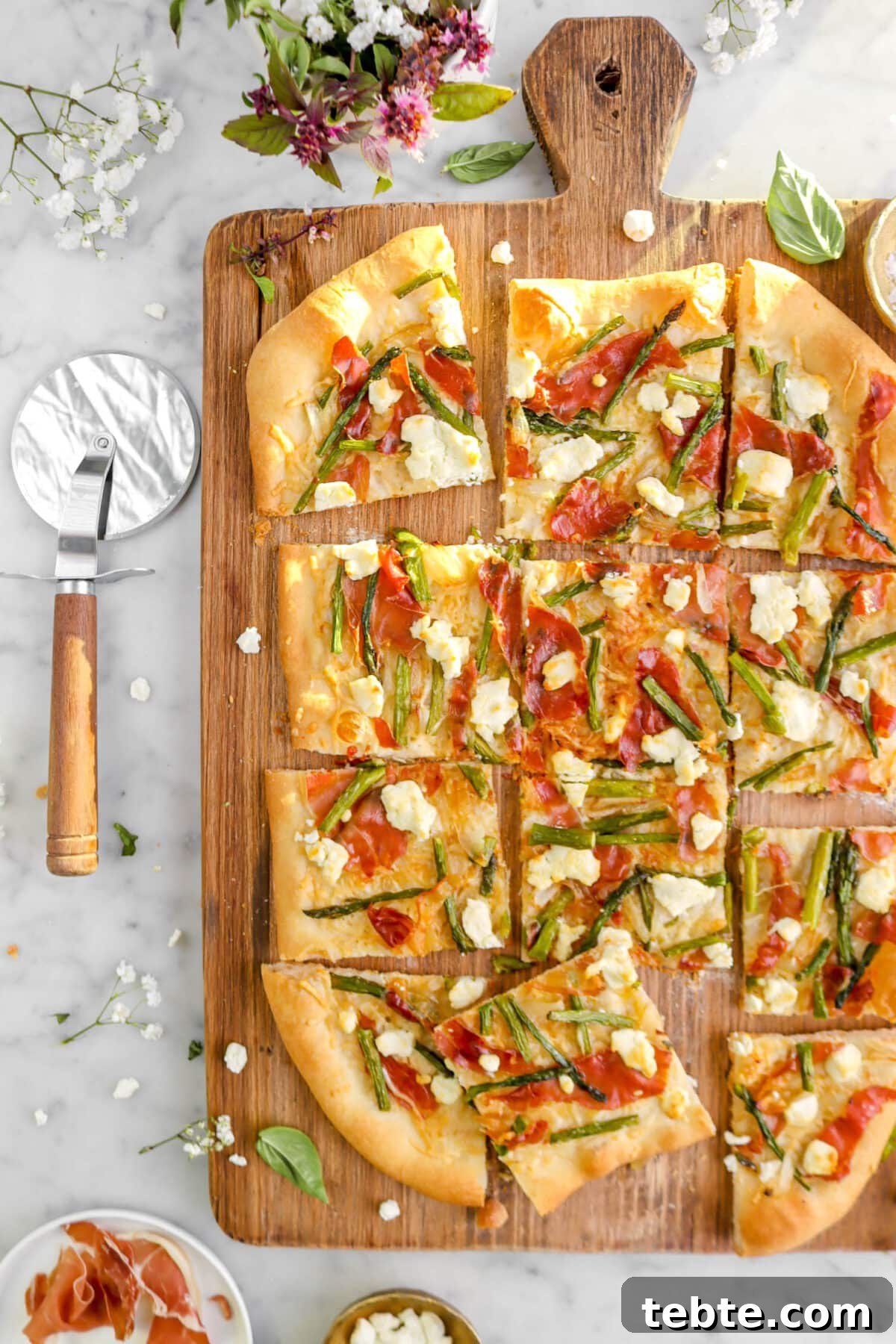 Asparagus, Caramelized Onion & Prosciutto Flatbread with Goat Cheese 5 cropped close up of sliced flatbread on wood board with pizza cutter beside.